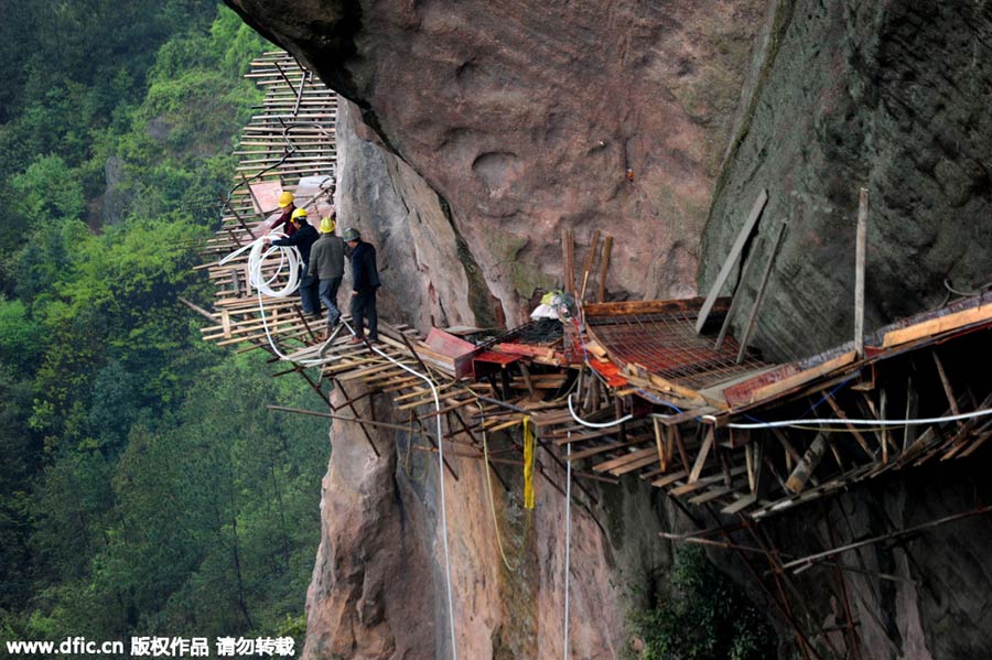 Workers balance on planks to build mountain road