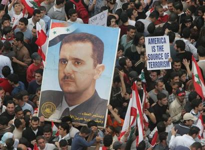 Pro-Syrian protesters carry a big portrait of Syrian President Bashar Assad, left, and anti-American placard, right, during a pro-Syrian demonstration in Beirut, Lebanon, Tuesday March 8, 2005. The protest, organized by the Shiite Muslim militant group Hezbollah, is meant to counter the almost daily anti-Syrian protests staged by the Lebanese opposition that had drawn tens of thousands. [AP]