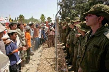 Opponents to Israeli Prime Minister Ariel Sharon's disengagement plan (L) dance in front of Israeli soldiers (R) as they secure the fence of Kfar Maimon July 20, 2005. 