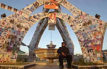 An Afghan policeman sits under a column adorned with posters of candidates for the forthcoming parliamentary elections, in the western Afghan city of Herat September 13, 2005. [Reuters]