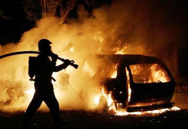 A firefighter extinguishes a car in 'Les Musicians' housing complex of Les Mureaux, north west of Paris, Saturday, Nov. 5, 2005 on the tenth day of unrest. Vehicles and buildings were torched by youths in largely immigrant areas who began rampaging after two of their peers were electrocuted last week at a power substation while hiding from police they feared were chasing them. (AP 