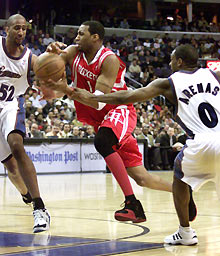 Tracy McGrady (C) of the Houston Rockets gets fouled by Gilbert Arenas (R) of the Washington Wizards while trying to drive the lane to the basket between Arenas and Wizards Calvin Booth during the second half of their NBA game in Washington January 3, 2006.