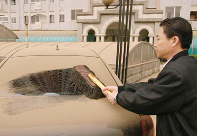 A man sweeps dust off his car parked in the open air near his home in Beijing April 17, 2006. [Xinhua] duststorm, weather, sandstorm, blue sky