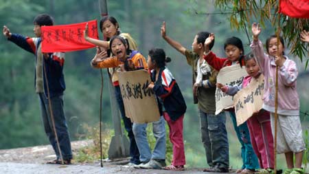 Children holding placards wave to the passing-by rescuers to express their gratitude beside the road linking the quake-devastated Qingchuan and Guangyuan of southwest China's Sichuan Province, May 21, 2008.