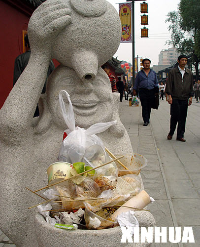 A stone statue with a bowl is full of rubbish dropped by passerby