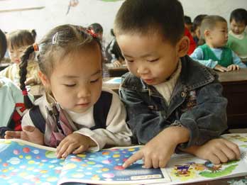Ye Zijuan (right) and Tang Yule, both five years old, read a children's magazine at a pre-school class for migrant children in Wenling, Zhejiang Province. Schooling for migrant children still remains a problem even though governments have urged the temporary schooling fee to be scrapped. [newsphoto]