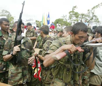 A Colombian paramilitary of the United Self-Defense Forces of Colombia kisses his weapon (R) before turning it over to authorities, during a demobilization in Turbo, Antioquia province, November 25, 2004. Paramilitary units demobilized and handed over their weapons as part of the peace process with the Colombian government. [Reuters]