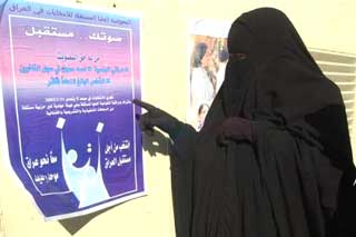 An Iraqi woman reads election posters in the southern Iraqi town of Basra Tuesday Nov. 30, 2004. Iraqi Prime Minister Ayad Allawi will travel to Jordan on Tuesday to meet with Iraqis outside the country as part of attempts to get as many Iraqis as possible to participate in upcoming elections. (AP 