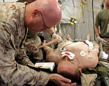 U.S. Navy Lieutenant Kenneth Nielson, a Catholic chaplain with the 1st Force Service Support Group, reads a prayer from "Rite for the anointing of the sick" for a wounded Marine being treated at the Surgical/Shock Trauma Platoon at Camp Taqaddum, after he was injured during combat operations against insurgents in the western Iraqi city of Falluja, in this photograph released on December 8, 2004. In the first six days of the U.S.-led offensive, the 63 surgeons, nurses, corpsmen, and other personnel of the Surgical Shock Trauma Platoon treated 157 patients and performed 73 operations. [Reuters]