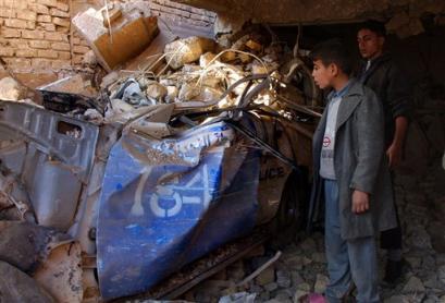 People look at a damaged patrol car covered by rubble of houses destroyed in a blast in west Baghdad Wednesday Dec. 29, 2004. Insurgents lured police to a house in west Baghdad with an anonymous tip about a rebel hideout Tuesday night, then set off explosives, killing at least 29 people and wounding 18, police said Wednesday. Seven policemen were among the dead. [AP]