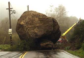 A boulder some 25 feet high blocks both lanes of the Topanga Caynon Road, Monday, Jan. 10, 2005, as electrical contractors fix broken power and communication lines in Malibu, Calif. No injures where reported, but the road remains closed. The storm system was blamed for at least nine deaths during the weekend in Southern California, including a man killed when his vehicle plunged into the surf off Pacific Coast Highway in Malibu, and a homeless man killed when the hillside where his tent was pitched gave way. [AP]