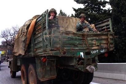 Two Syrian soldiers sit on their military truck carrying ammunition enroute to the Syrian border in Bekaa Valley east of Beirut, Lebanon, Sunday March 27, 2005. Syrian troops vacated positions in eastern Lebanon Sunday. Some 35 military trucks loaded with soldiers, equipment, ammunition boxes and some towing 14 antiaircraft guns crossed into Syria at the Masnaa border crossing in eastern Lebanon late Sunday, witnesses said. [AP]
