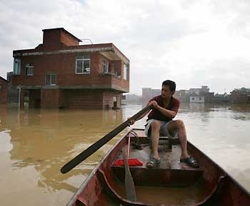 A Chinese man uses a boat to make his way in a flooded neighbourhood in Wuzhou, southwest China's Guangxi Zhuang Autonomous Region June 25, 2005. [Reuters]