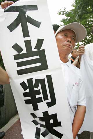 68-year-old Wang Jinhua holds a banner after a legal judgement in front of the Tokyo High Court in Tokyo July 19, 2005. A Tokyo court on Tuesday rejected demands from Chinese plaintiffs for compensation and an apology from Japan's government for biological warfare conducted in China before and during World War Two. The banner reads, "Unjust Ruling"/ 