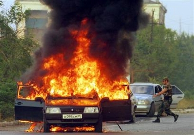 An armed man runs toward a burning car, set ablaze by unidentified gunmen who opened fire on the car in the Chechen capital Grozny, Tuesday, Aug. 9, 2005.