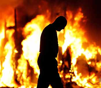 A man walks past a burning vehicle in a Loyalist area in North Belfast September 12, 2005. Belfast ground to a halt on Monday evening after Protestant demonstrators blocked roads and nervous commuters, fearing a resumption of the weekend's rioting, scrambled to leave the city early. [Reuters]