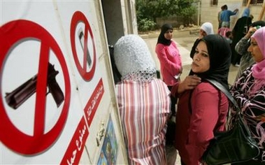 A sign bans firearms and mobile phones as women line-up to vote in municipal elections at a polling station in the West Bank village of Beit Fagar near Bethlehem, Thursday, Sept. 29, 2005.