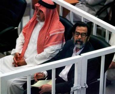 Saddam Hussein wears glasses as he takes notes on a pad of paper beside fellow defendant Awad Hamad al-Badar at their trial held under tight security in Baghdad's heavily fortified Green Zone in Iraq October 19, 2005. [Reuters]