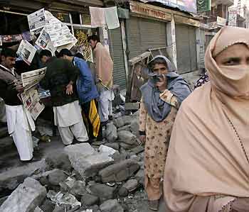 Kashmiri earthquake survivors walk past a reopened newspaper stand in Muzaffarabad, capital of Pakistani-administered Kashmir October 22, 2005. [Reuters]