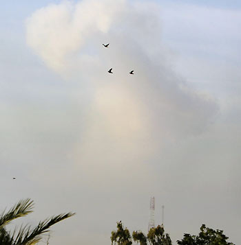 Three birds fly in front of a column of smoke rising over Baghdad after two early morning explosions November 18, 2005.