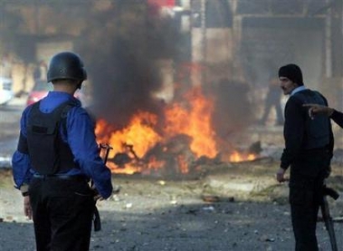 Iraqi policemen look at the burning wreckage of a car bomb that exploded near a two-car convoy carrying foreigners through central Baghdad, Iraq, Saturday, Nov. 26, 2005, killing four Iraqi civilians.