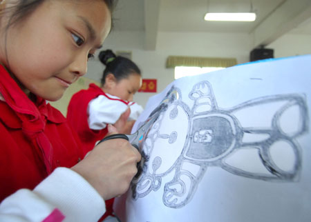 A student cuts out the likeness of Fuwa Bei Bei the Fish, a mascot for the Beijing Olympic Games, in a Nanchang primary school in East China&apos;s Jiangxi Province, March 31, 2008. The school encouraged students to make Fuwa-themed paper-cuts to celebrate the upcoming Olympics. [Xinhua]