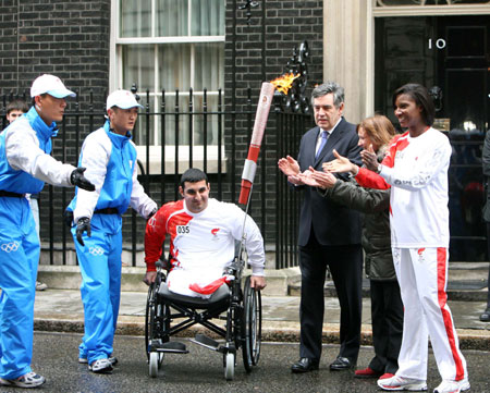 Britain's Prime Minister Gordon Brown (3nd R) claps as physically-challenged athlete Ali Jawad (3nd L) receives the Beijing Olympic torch outside 10 Downing Street in London April 6, 2008. The Beijing Olympic torch relay proceeds in London, which will be the largest city relay outside the Chinese mainland. [Xinhua]