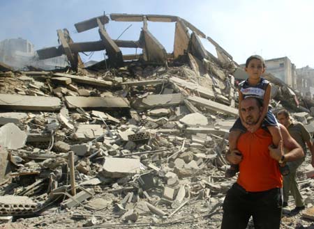 A Lebanese man carries his son on shoulders as walks next a destroyed building in the southern Beirut suburbs August 14, 2006.