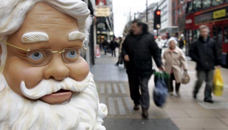 hoppers pass a plastic singing Santa Claus on Oxford Street, London's main shopping street, December 24, 2006. 