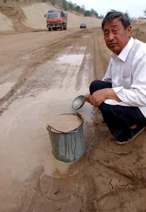 A Chinese farmer collects rainfall water converged on a road in Huan County, Southwest China's Gansu Province, May 22, 2007. The rainfall water after simple treatment will be used as the drinking water for the farmer's family. The Huan County suffered drought since September 2004 and there has been no effective rainfall for the past 32 months, Xinhua said.[Xinhua]