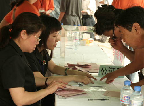 Two notary officials check the documents of voters at the venue for a vote on demolishment and reconstruction of old buildings in Juixiaqiao Sub-district in Beijing, June 9, 2007. Local government and the real estate developer jointly organize the vote on Saturday to see if majority residents of over 5000 families accept the new compensation policy after failed attempts to reach an agreement through other ways. Both notary officials and supervisors are invited to monitor the vote that runs from 9 a.m. to 9 p.m. at six ballot booths. [Sun Yuqing/www.chinadaily.com.cn]