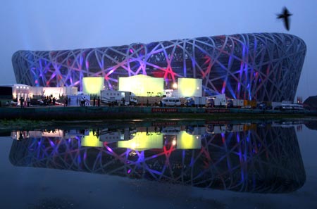 A bird flies over the National Olympic Stadium, also known as the Bird's Nest, which is lit by coloured lights during activities to mark a one year countdown to the 2008 Olympic Games at night in Beijing, August 5, 2007. The Chinese capital is gearing up to celebrate the one year countdown to the opening ceremony of the 2008 Olympic Games on August 8.