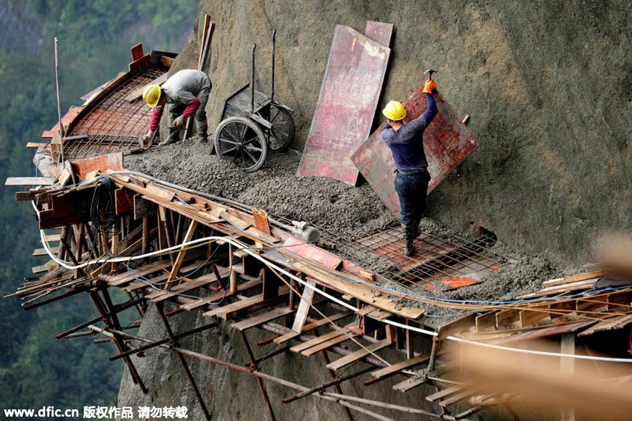 Workers balance on planks to build mountain road