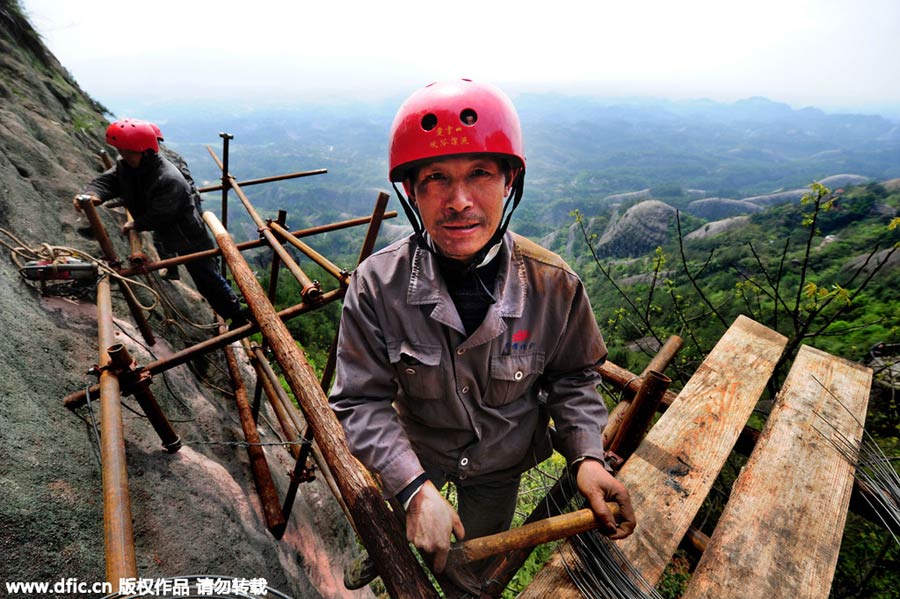 Workers balance on planks to build mountain road