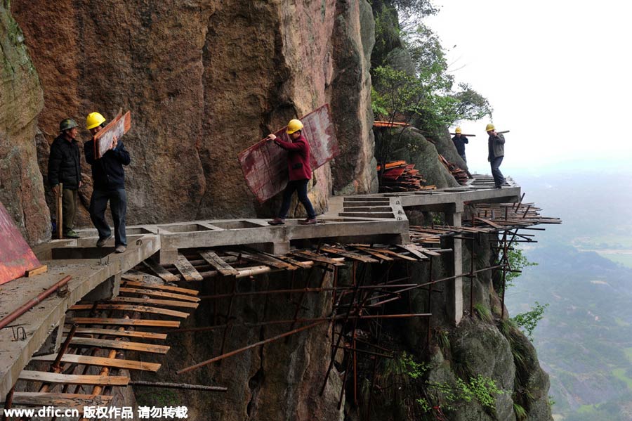 Workers balance on planks to build mountain road