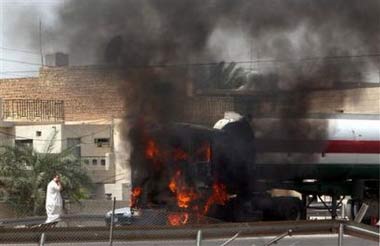 An oil tanker is seen engulfed with fire as its driver, left, talks on a mobile phone, in western Baghdad, Iraq, Wednesday, March 22, 2006. The cause of the fire was not know but according to driver of the oil tanker, U.S. army fired at the tanker and set it ablaze. [AP]