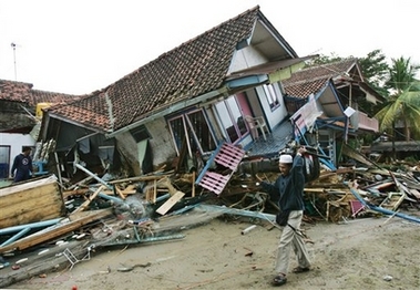 An Indonesian man carries his belongings as he walks past by a destroyed house at a tsunami-ravaged area in Pangandaran, West Java, Indonesia, Tuesday, July 18, 2006. Desperate villagers and soldiers dug through destroyed homes and hotels looking for survivors Tuesday of a tsunami on Indonesia's Java island, as the death toll rose to at least 262, officials and media reports said. 