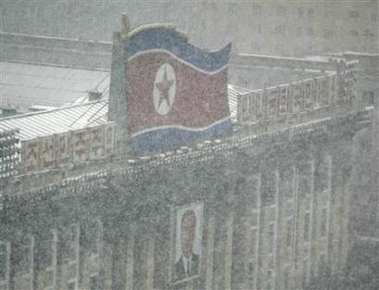 A portrait of late North Korean leader Kim Il-sung hangs under a North Korean flag as it snows in Pyongyang, December 19, 2006.