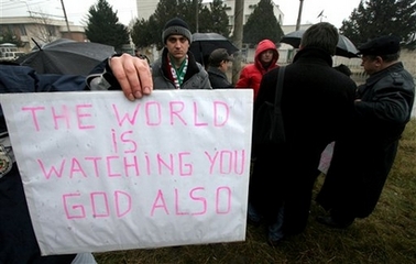 People protest behind a poster which reads 'The World watching You God also', during a protest in front of the Libyan embassy in the Bulgarian capital Sofia, Tuesday, Dec. 19, 2006.