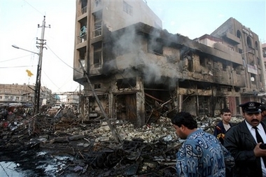 Iraqis stand next to a building heavily damaged in a car bomb explosion in Baghdad, Iraq, Sunday, Feb. 18, 2007.