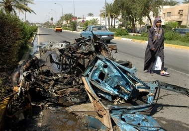 A woman passes by a wreck of a car destroyed in a suicide car bomb attack in Baghdad, Iraq, Wednesday, March 14, 2007.
