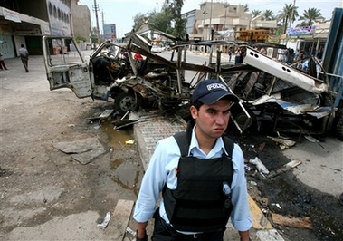 Iraqi policeman stands in front of a mini bus destroyed after a suicide bomber blew himself up in northwest Baghdad, Iraq, Sunday, April 15, 2007.